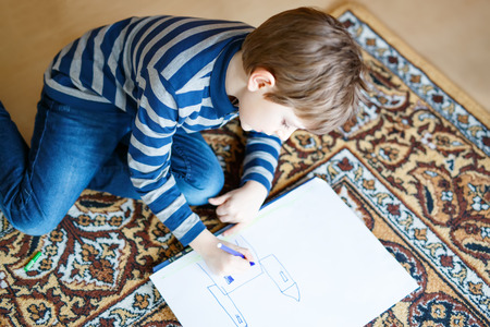 preschool kid boy at home making homework, painting a story with colorful pensの写真素材
