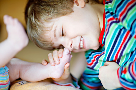 Little kid boy kissing and playing with foot of newborn baby.の写真素材