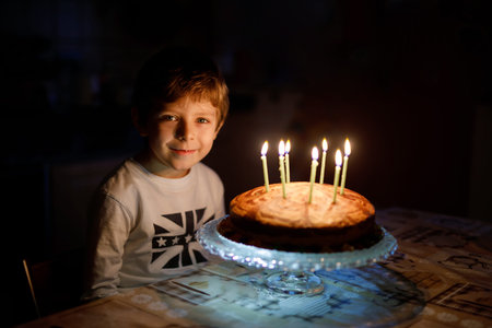 Child blowing seven candles on homemade baked cake, indoor.の写真素材