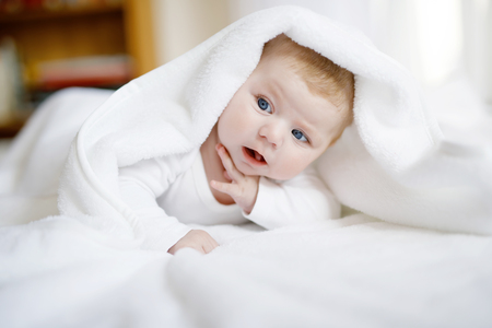 Baby girl wearing white towel or winter overal in white sunny bedroomの写真素材
