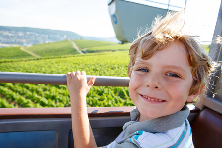 Smiling happy blond littlekid boy in cable funicular over vineyards in summerの写真素材