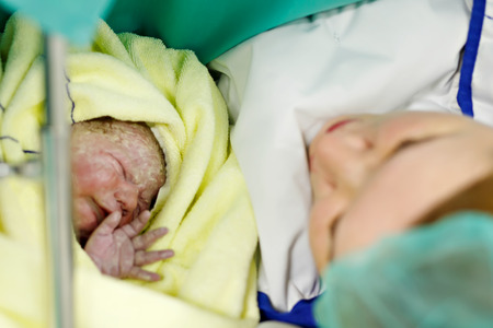 Newborn baby wrapped in blankets after birth. Mother looking for the first time on new born daughterの写真素材