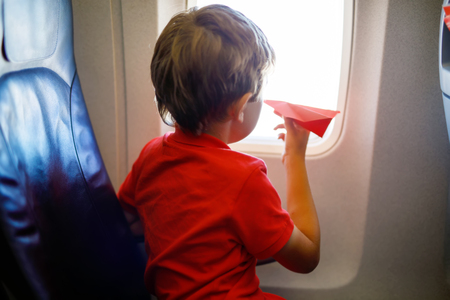 Little kid boy playing with red paper plane during flight on airplaneの写真素材