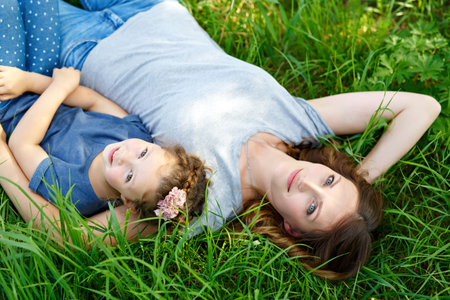 Beautiful young mother and little daughter lying on green grass and restingの写真素材