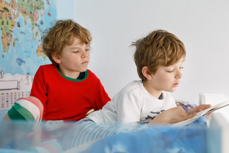 Two little kids boys in pajamas reading a book in bed.の写真素材