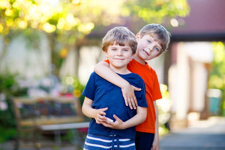 Two little active school kids boys, twins and siblings hugging on summer dayの写真素材