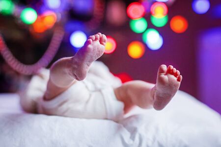 newborn baby feet and diaper with Christmas tree and colorful garland lightsの写真素材