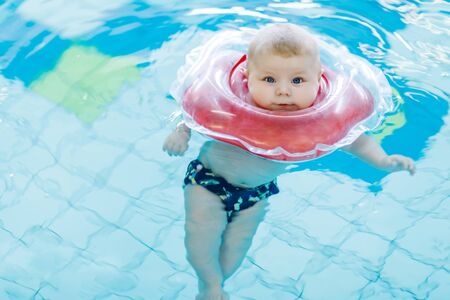 Cute little baby child learning to swim with swimming ring in an indoor poolの写真素材