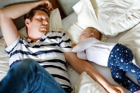 Cute adorable baby girl of 6 months and her father sleeping peaceful in bed at homeの写真素材