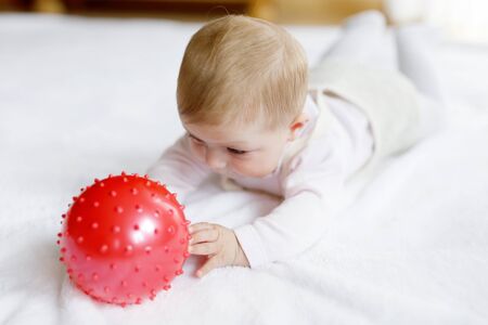 Cute baby playing with red gum ball, crawling, grabbingの写真素材