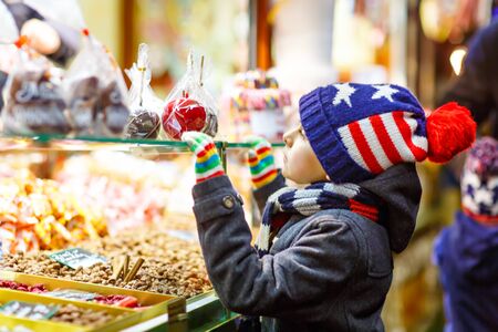 Little kid boy with gingerbread and sweets stand on Christmas marketの写真素材