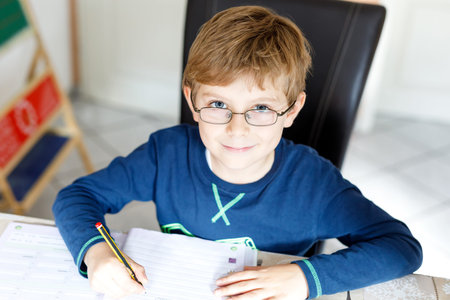 Happy school kid boy at home making homework