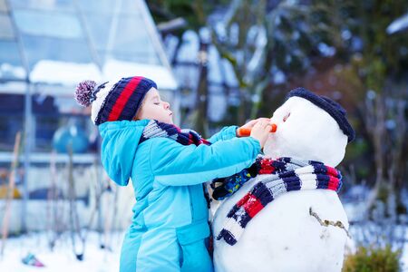 Funny kid boy making a snowman in winterの写真素材