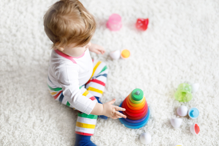 Adorable cute beautiful little baby girl playing with educational colorful wooden rainboy toy pyramidの写真素材
