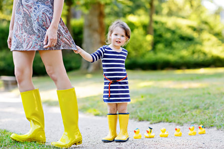 Mother and little adorable toddler child in yellow rubber boots, family look, in summer park. Beautiful woman and cute girl daughter walking togetherの写真素材
