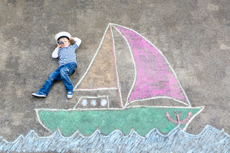 Little kid boy as pirate on ship or sailingboat picture painting with colorful chalks on asphalt.の写真素材