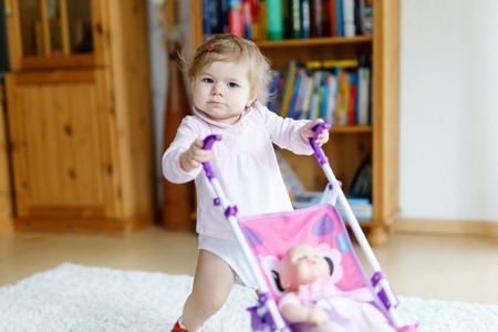 Cute adorable baby girl making first steps with doll carriage.の写真素材