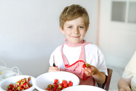 Little blond kid boy helping and making strawberry jam in summerの写真素材