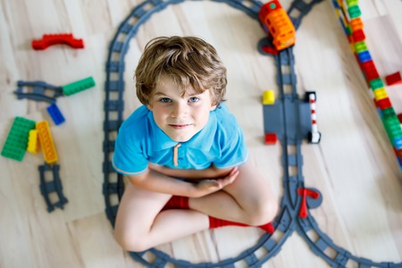 little blond kid boy playing with colorful plastic blocks and creating train stationの写真素材