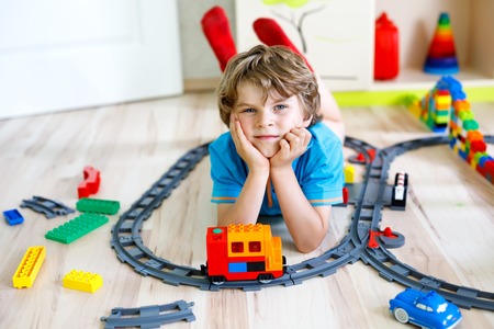 little blond kid boy playing with colorful plastic blocks and creating train stationの写真素材