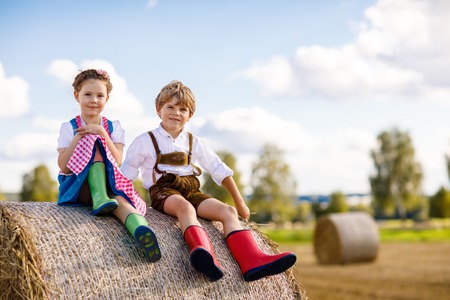 Adorable little kid boy and girl in traditional Bavarian costumes in wheat field on hay stackの写真素材