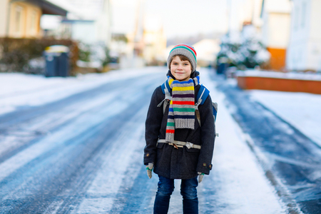 Happy kid boy with backpack or satchel having fun with snow on way to schoolの写真素材