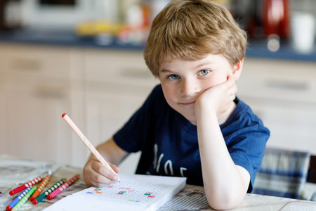 Happy smiling kid boy at home making homework writing letters with colorful pensの写真素材