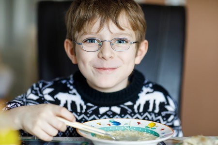 Beautiful little school boy eating vegetable soup indoor.の写真素材