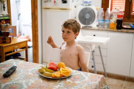 Cute little kid boy eating lots of different fruits in home kitchen in summerの写真素材