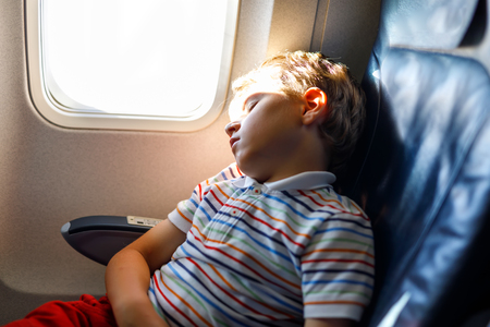 Little kid boy sleeping during long flight on airplane. Child sitting inside aircraft by a windowの写真素材