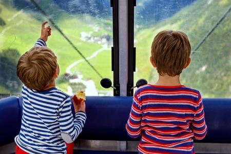 Two little boys sitting inside of cabin of cable car and looking on mountains landscape.の写真素材