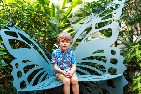 Little blond preschool kid boy discovering flowers and butterflies at botanic gardenの写真素材