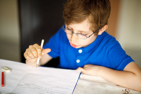 Cute little kid boy with glasses at home making homework, writing letters with colorful pens.の写真素材