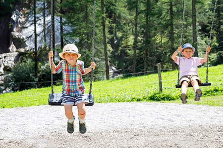 Funny kid boy having fun with chain swing on outdoor playground while being wet splashed with waterの写真素材