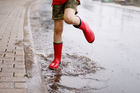 Child wearing red rain boots jumping into a puddle.の写真素材