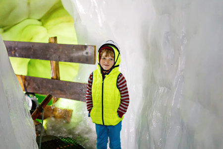 Little kid boy with safety helmets inside of glacier with ice tunnel. Schoolkid hiking and...