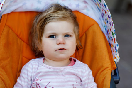 Portrait of little cute toddler girl sitting in stroller or pram and going for a walk. Happy cute...