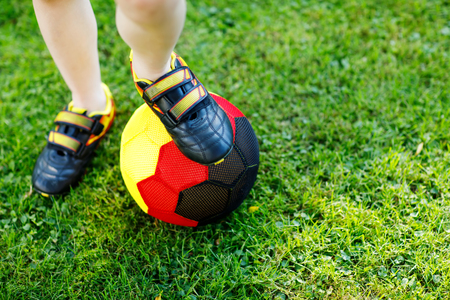 Close-up of feet of kid boy with football and soccer shoes in German national colors - black, gold and red. World or europe cup concept.の写真素材