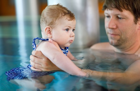 Happy middle-aged father swimming with cute adorable baby girl in swimming pool.の写真素材