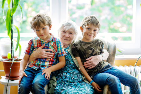 Happy family portrait with grandmother and two grandsons. Grand grandmother sitting with two school kid boys at homeの写真素材