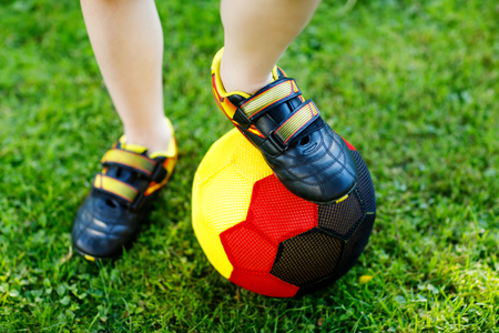Close-up of feet of kid boy with football and soccer shoes in German national colors - black, gold and red. World or europe cup concept.の写真素材