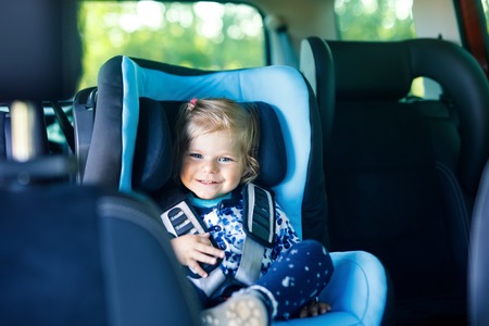 Adorable baby girl with blue eyes sitting in car safety seat. Toddler child going on family vacations and jorney. Smiling happy child during traffic jamの写真素材