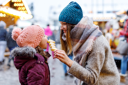Young mother and daughter eating white chocolate covered fruits on skewer on traditional German Christmas marketの写真素材
