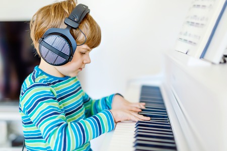 Cute healthy little kid boy playing piano in living room or music school. Preschool child having fun with learning to play music instrument. Education, skills conceptの写真素材