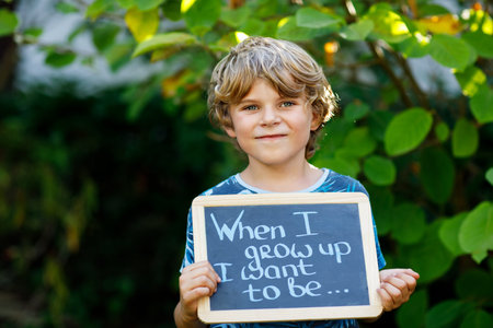 Happy little kid boy with chalk desk in hands. Healthy adorable child outdoors On desk When I grow...