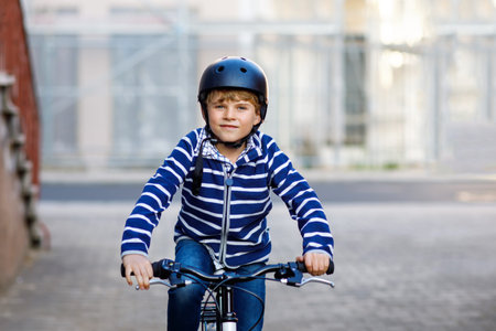 Schoolkid boy in safety helmet riding with bike in the city with backpack. Happy child in colorful clothes biking on bicycle on way to school. Safe way for kids outdoors to schoolの写真素材