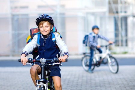 Two school kid boys in safety helmet riding with bike in the city with backpacks. Happy children in colorful clothes biking on bicycles on way to school. Safe way for kids outdoors to schoolの写真素材