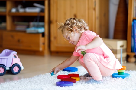 Adorable cute beautiful little baby girl playing with educational colorful wooden rainboy toy pyramidの写真素材