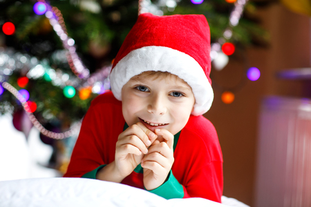 Little kid boy in santa hat with Christmas tree and lights on background.の写真素材