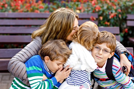 Mother and three children hugging. Happy family sitting outdoor: woman and two brother kids boys and cute little toddler girl. Siblings and mum in loveの写真素材